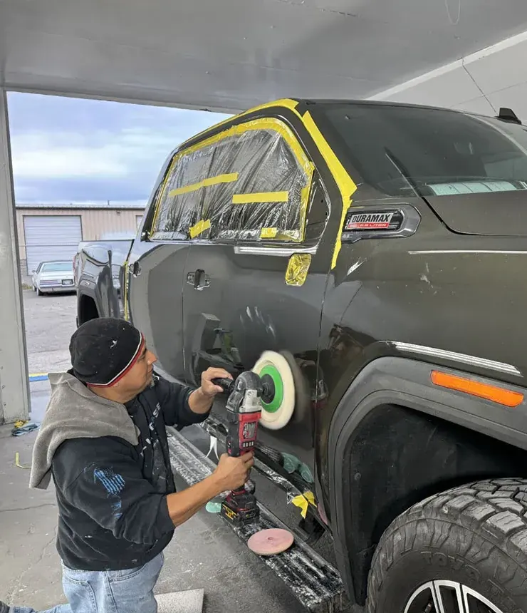 Technician machine-polishing the side of a dark pickup truck
